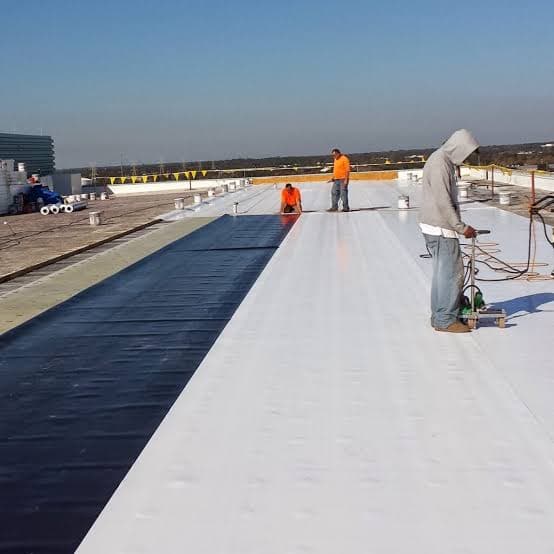Crew installing white TPO membrane on a commercial flat roof