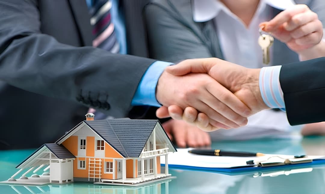 Real estate agent and buyer shaking hands over a house model, with keys being handed over
