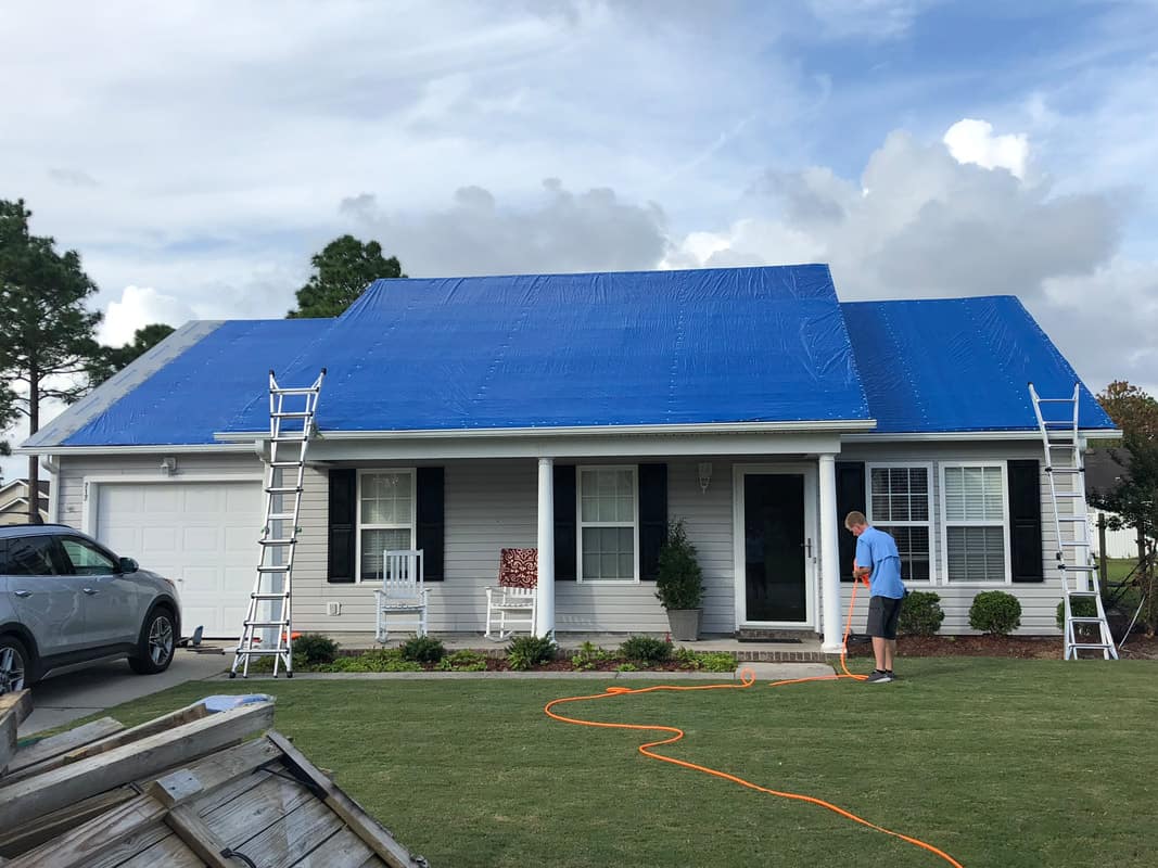 A residential roof fully covered in blue emergency tarp after storm damage