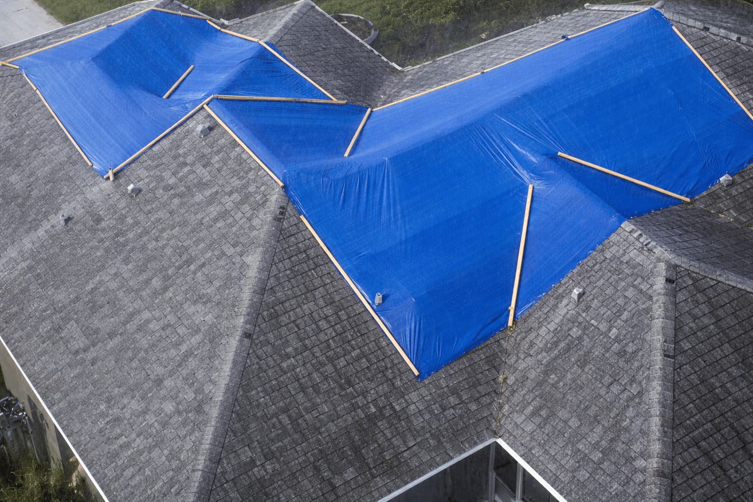 Aerial view of a complex roofline covered in blue emergency tarps during rain