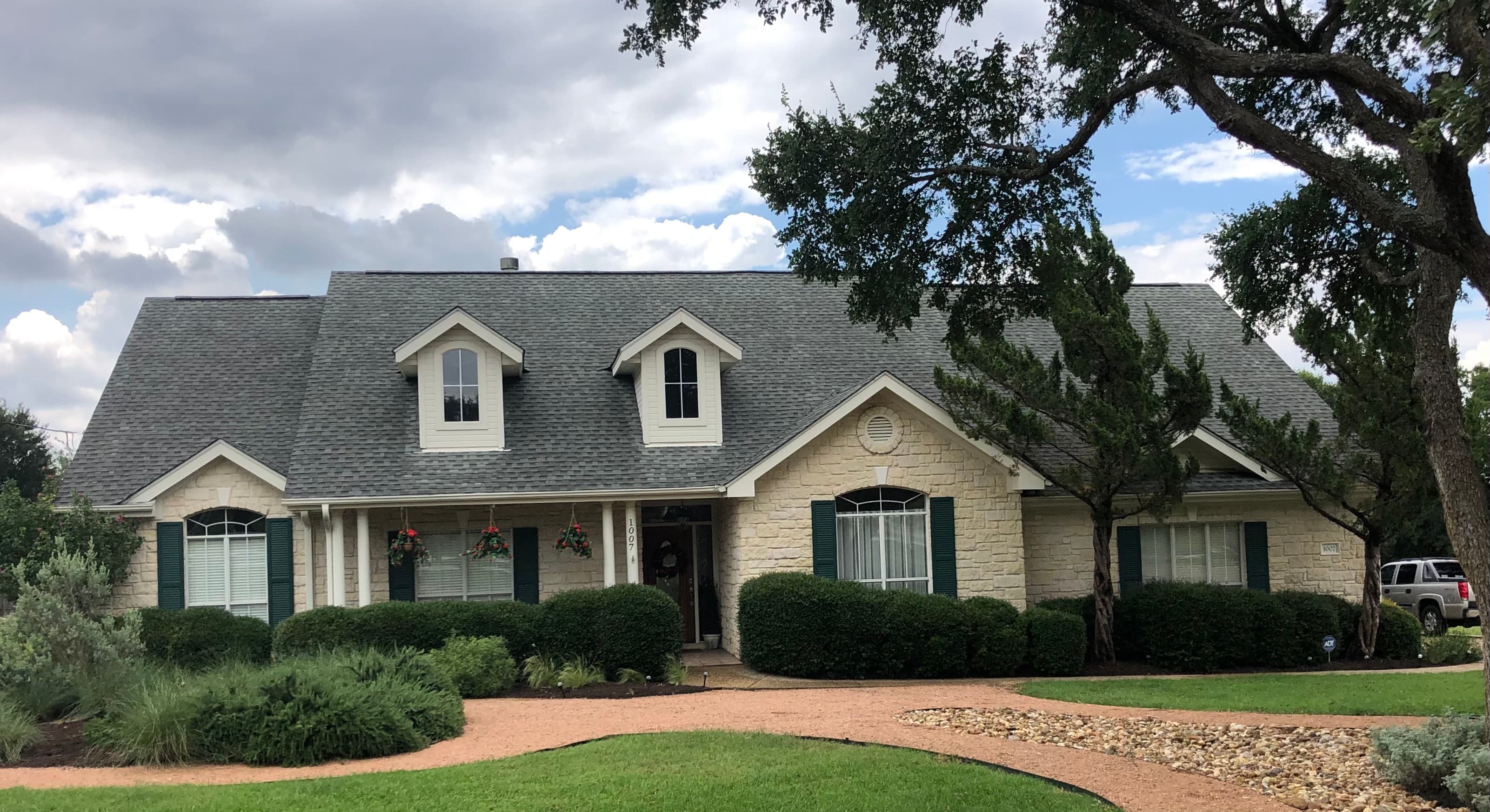 Stone Central Texas home with a newly installed grey architectural shingle roof and dormers