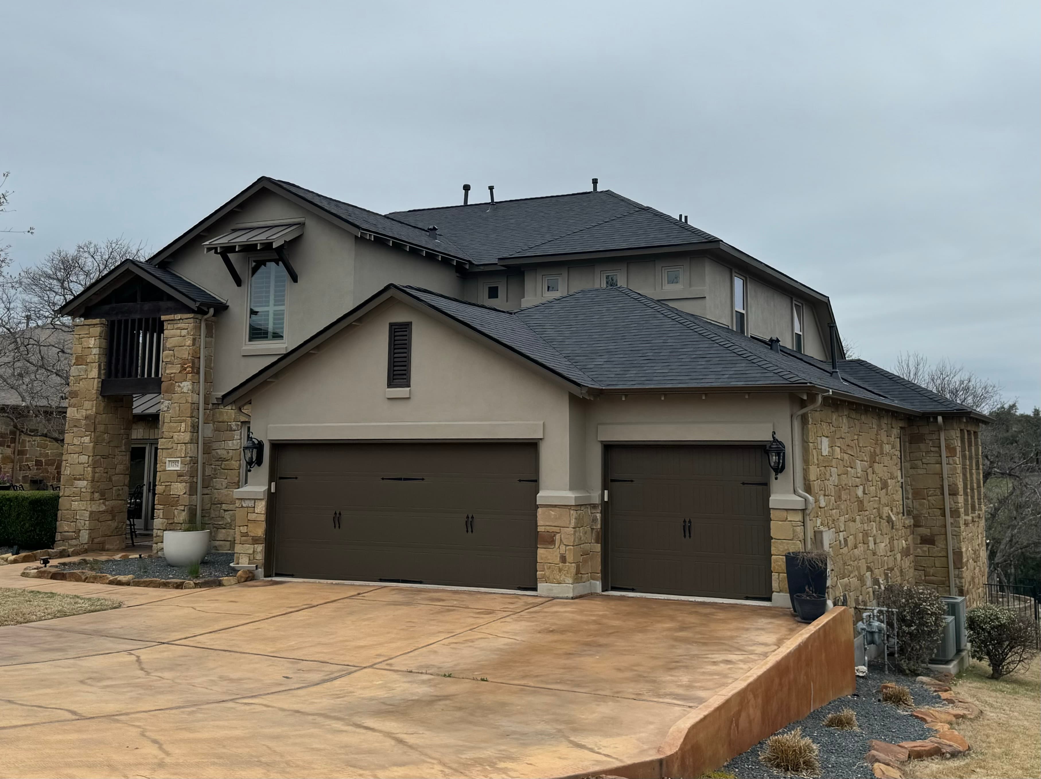 Two-story stone home with a dark grey architectural shingle roof