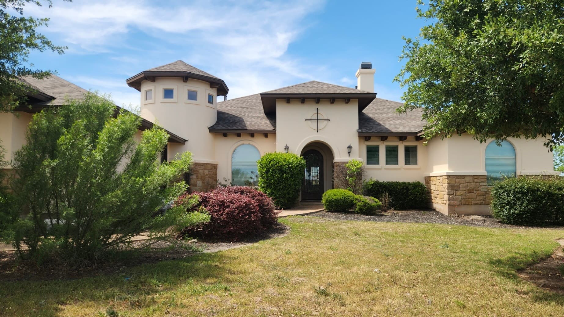 Cream stucco Hill Country home with a stone turret entry and dimensional shingle roof