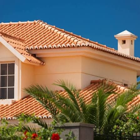 Stucco home with a terracotta clay tile roof and palm landscaping
